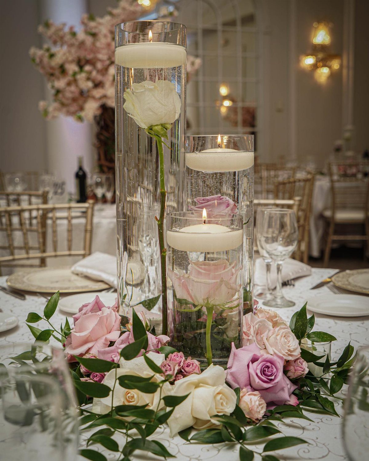 Glass cylinder vases with floating candles and submerged roses arranged as a floral centerpiece on a table.