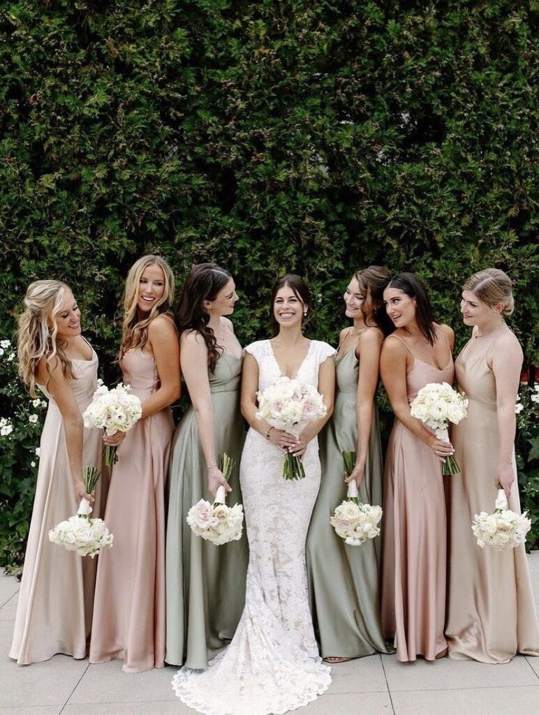 Bridesmaids in dusty rose and sage green dresses standing with a bride in white lace.