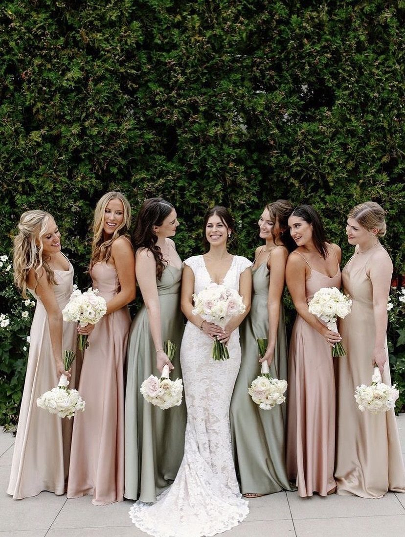 Bridesmaids in dusty rose and sage green dresses standing with a bride in white lace.