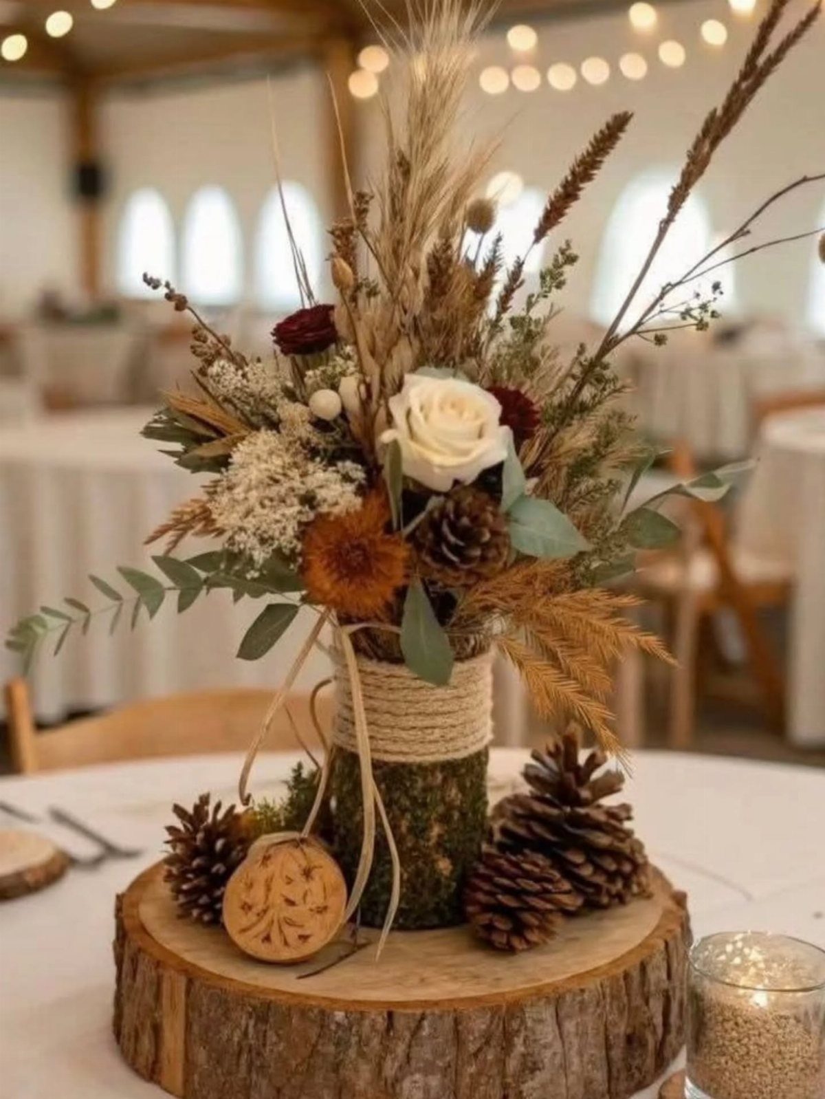 A rustic forest themed centerpiece with roses, pinecones, and dried florals on a wood slice base.