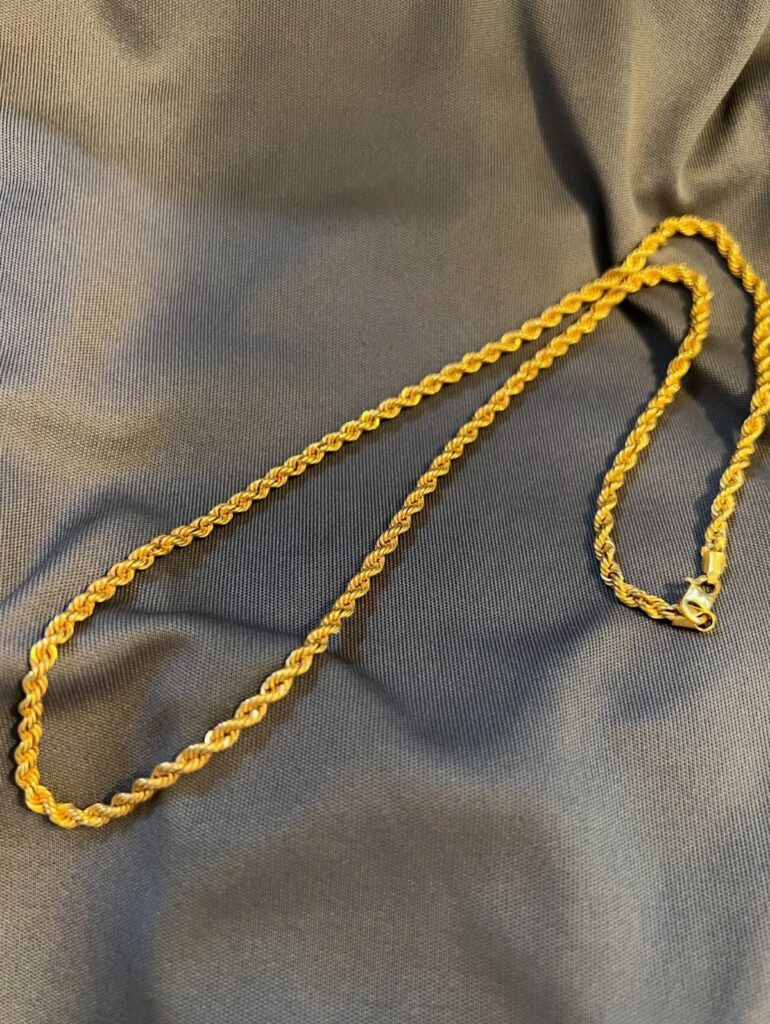 A gold rope chain necklace resting on a grey textured fabric surface.