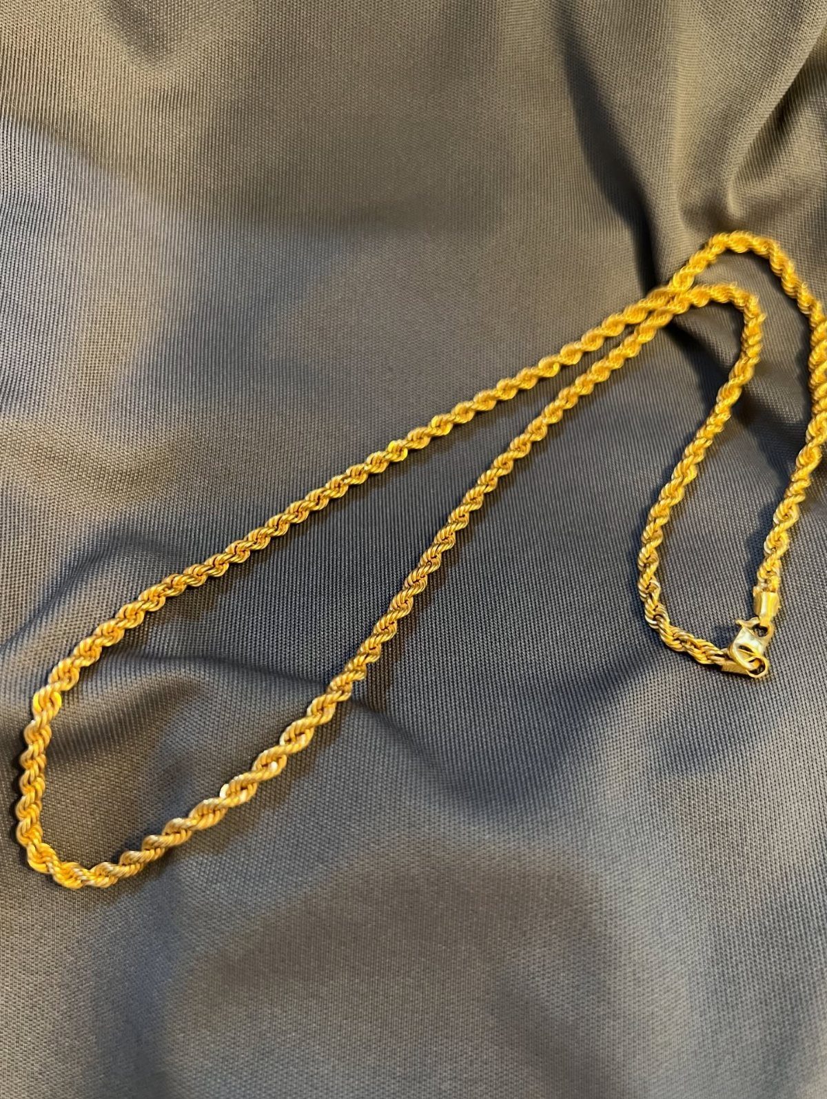 A gold rope chain necklace resting on a grey textured fabric surface.