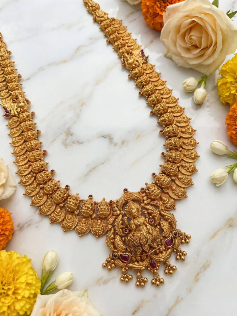 Intricate gold necklace with a central deity motif pendant resting on marble with flowers.