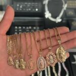 A hand holding several gold necklaces with various Virgin Mary religious pendants.