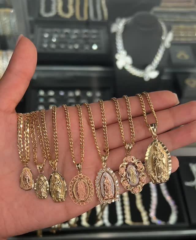 A hand holding several gold necklaces with various Virgin Mary religious pendants.