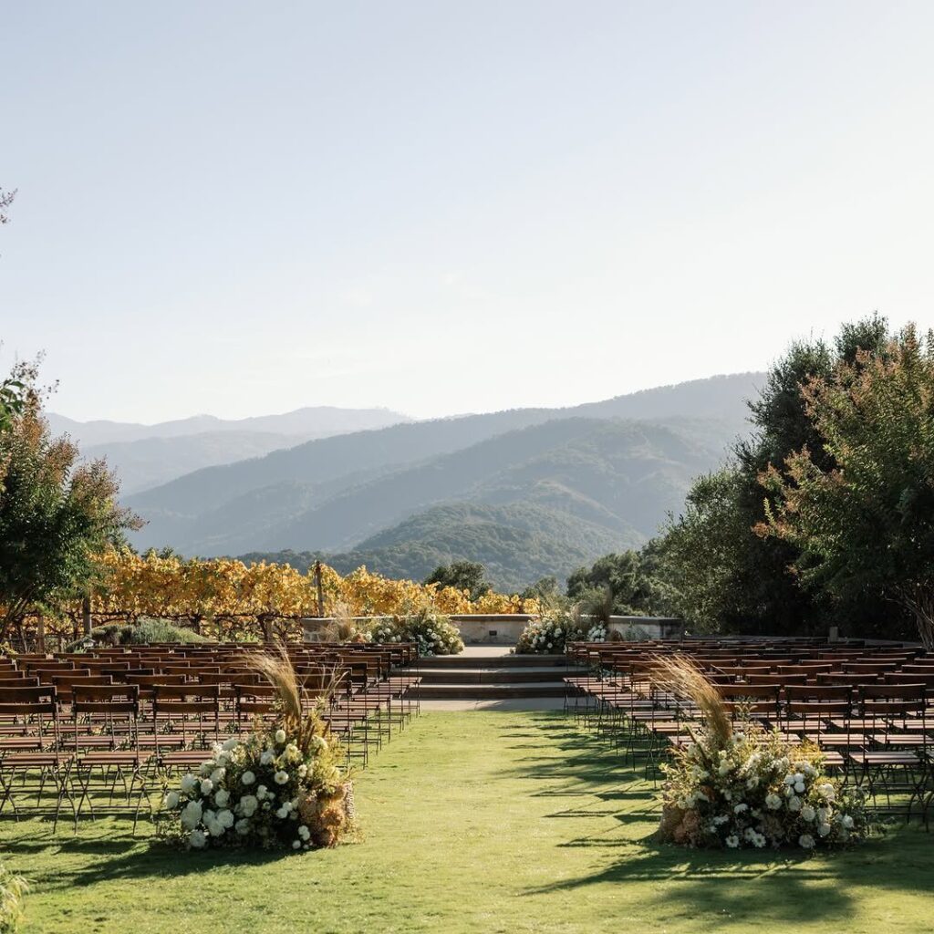 Wooden chairs arranged for an outdoor wedding ceremony overlooking mountains and a vineyard.