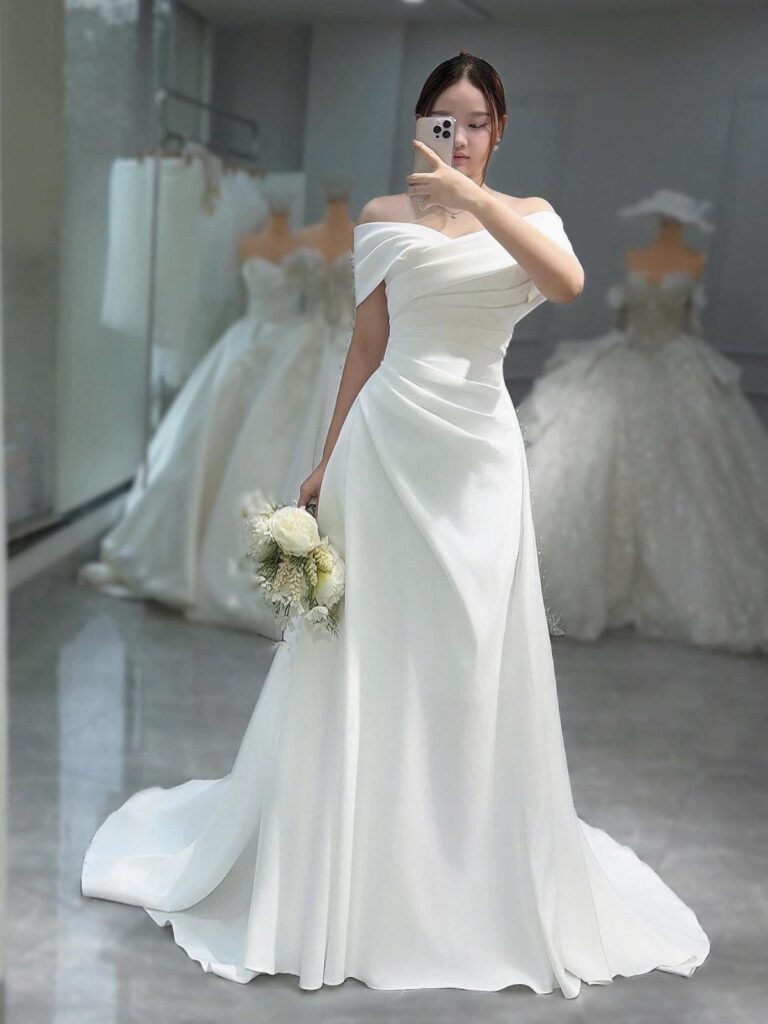 A woman in a white off-the-shoulder wedding gown holding a small flower bouquet.