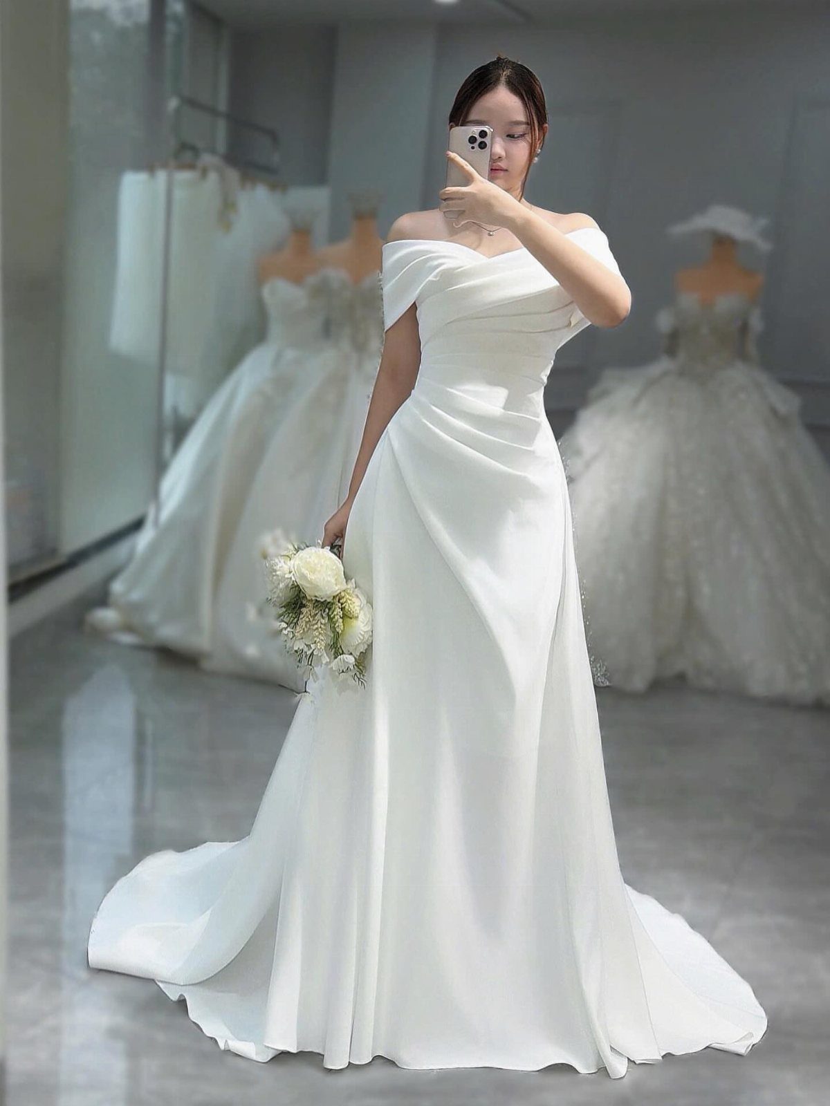 A woman in a white off-the-shoulder wedding gown holding a small flower bouquet.