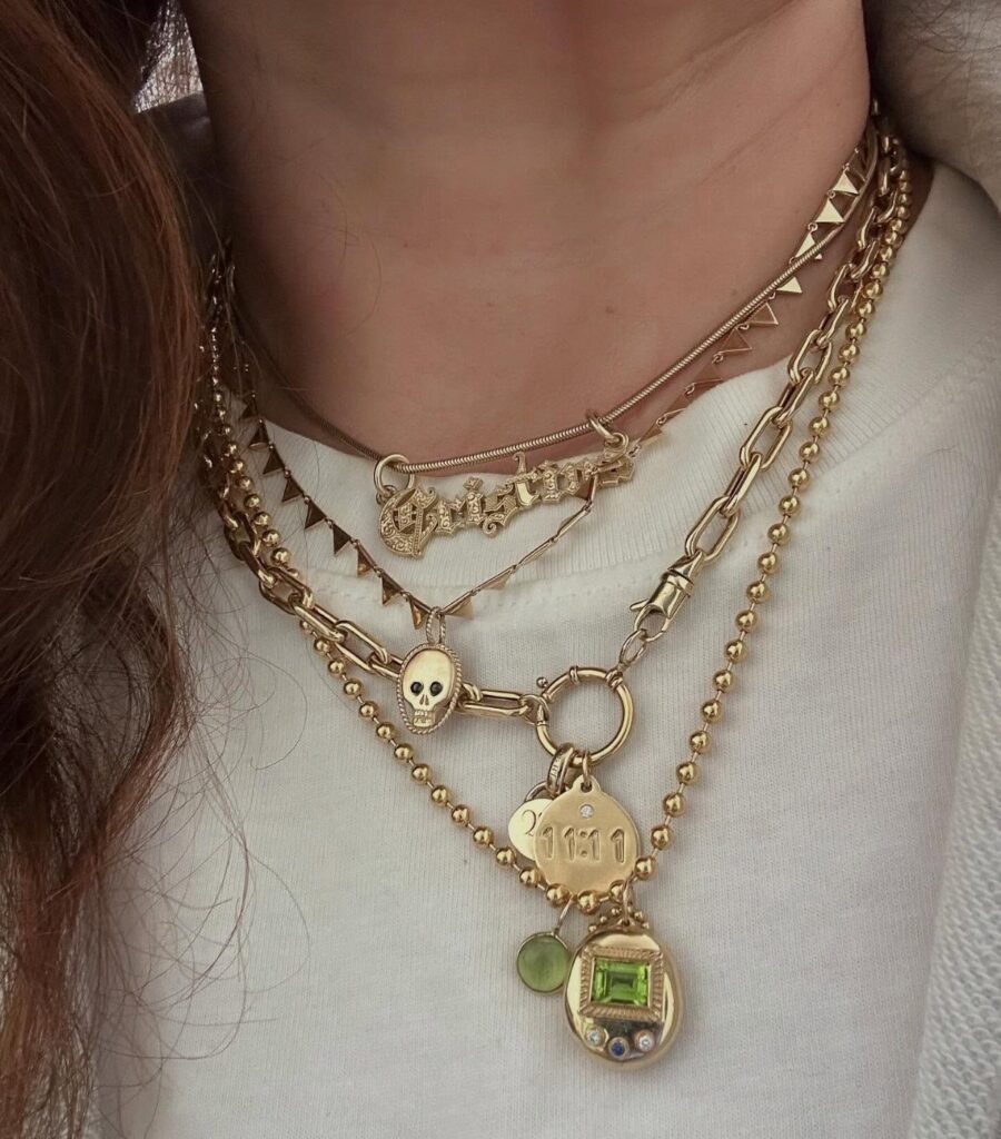 Multiple layered gold necklaces with various charms and textures worn around a person's neck.