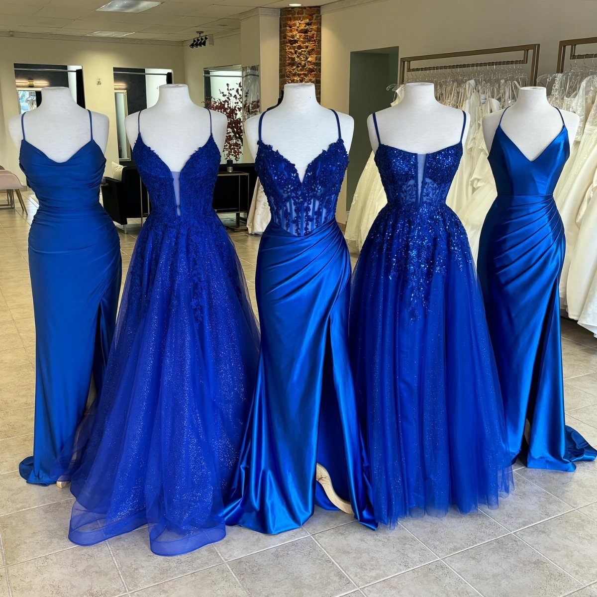 Five different styles of royal blue bridesmaid dresses displayed on white mannequins.