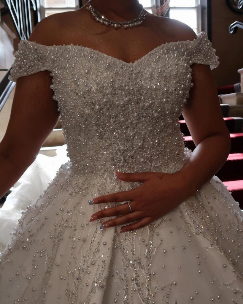 A person wearing a beaded white wedding dress and a pearl necklace.