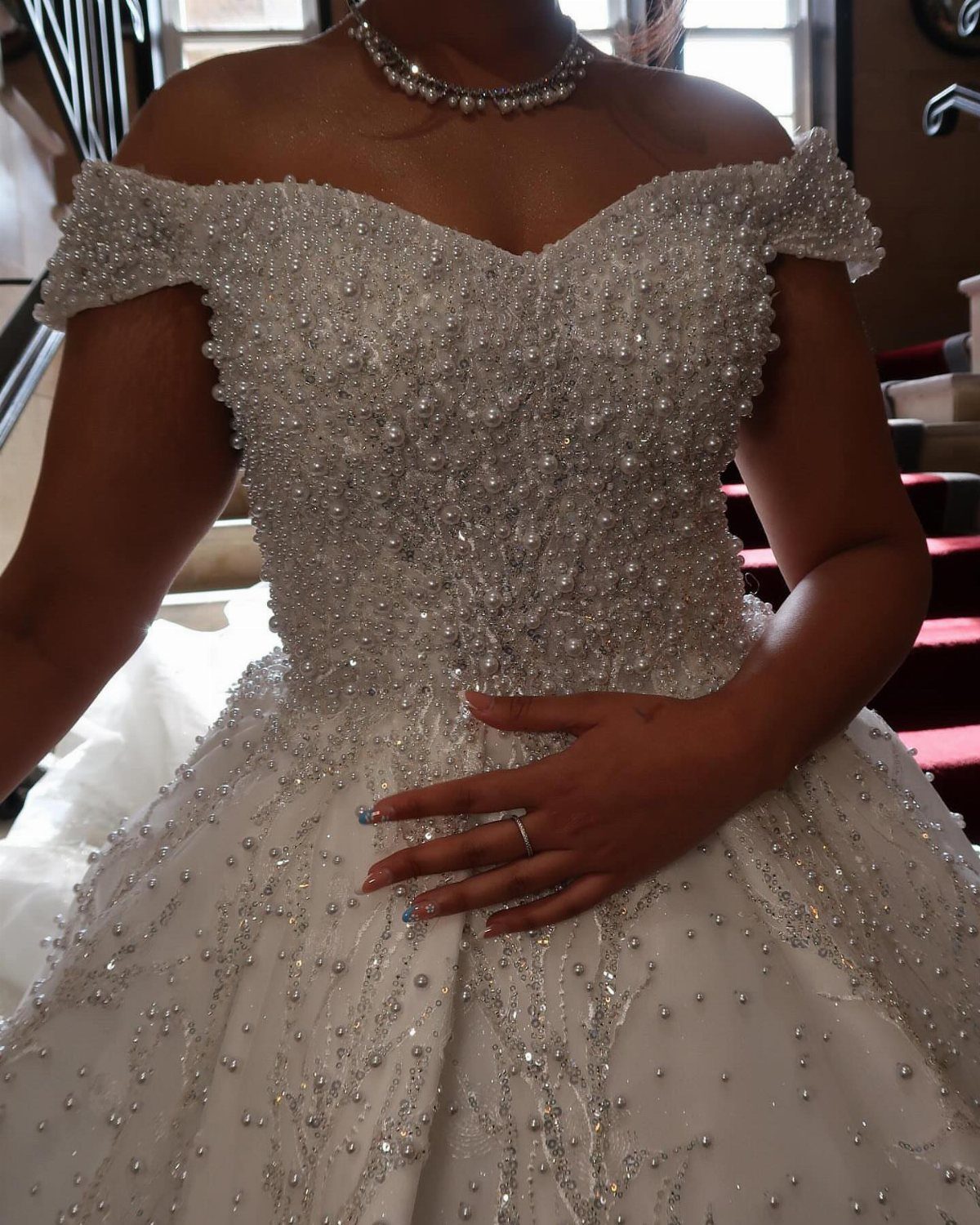 A person wearing a beaded white wedding dress and a pearl necklace.
