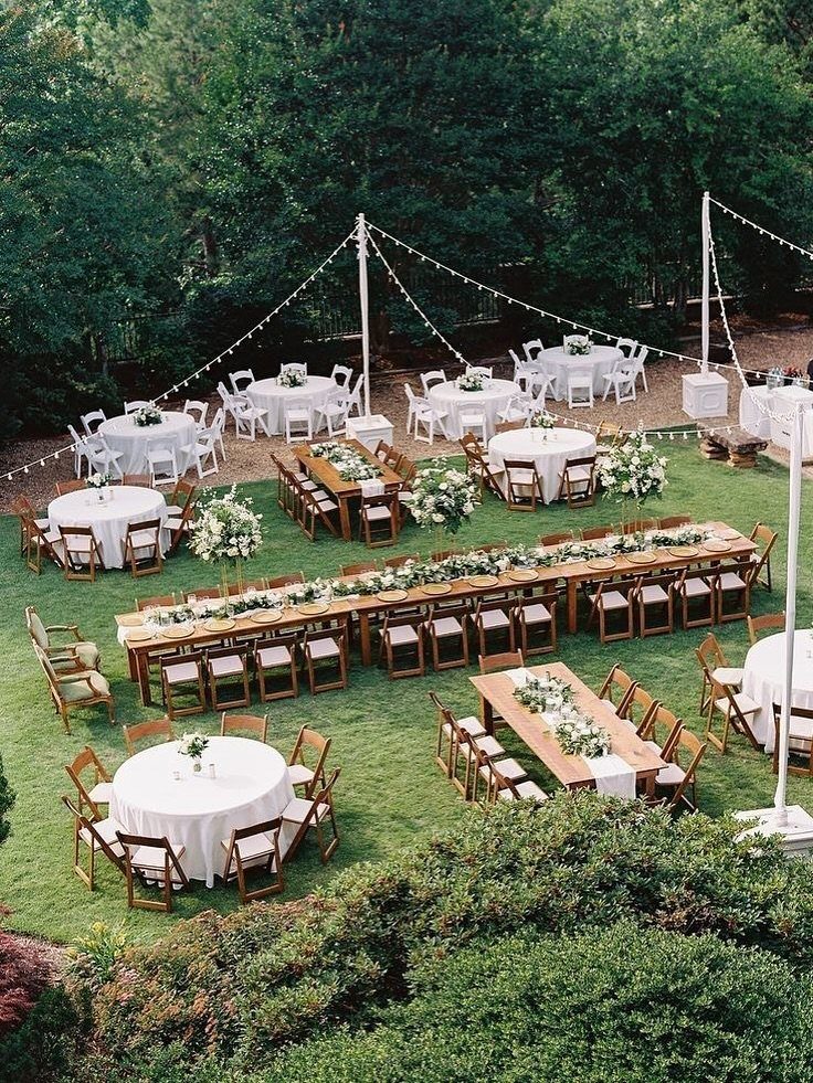 Outdoor wedding reception featuring round white tables and long wooden banquet tables on a green lawn.